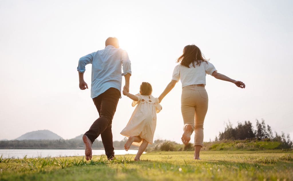 Happy family in the park sunset light. family on weekend running together in the meadow with river Parents hold the child hands.health life insurance plan concept